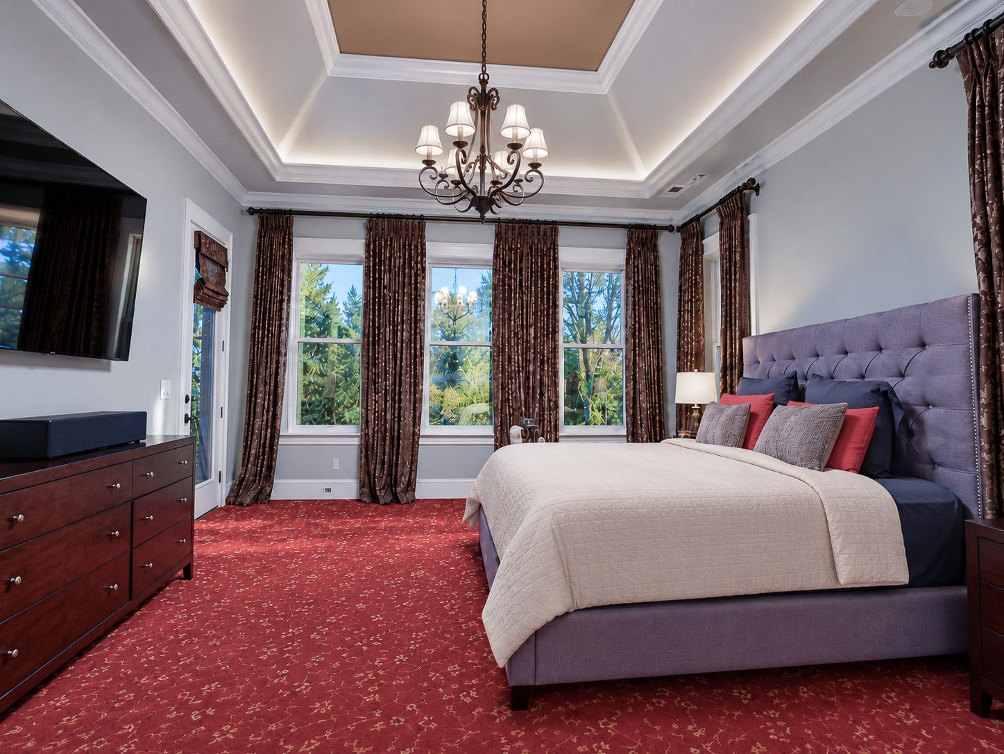 Primary bedroom with tray ceiling, chandelier and tall windows